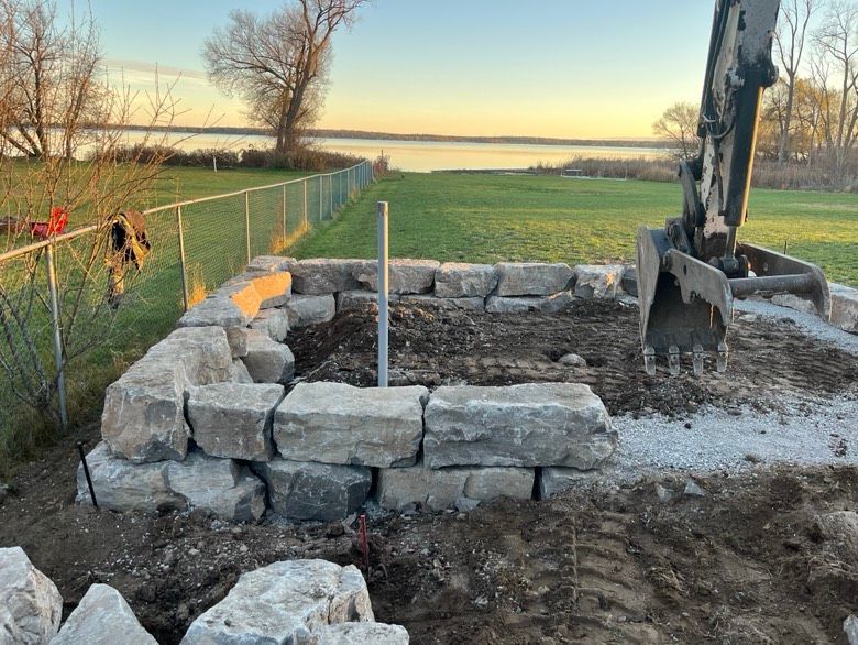 A large pile of rocks is being built in a field next to a body of water.