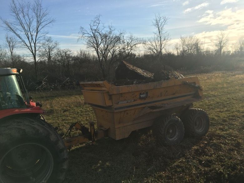 A tractor is pulling a dumpster in a field.