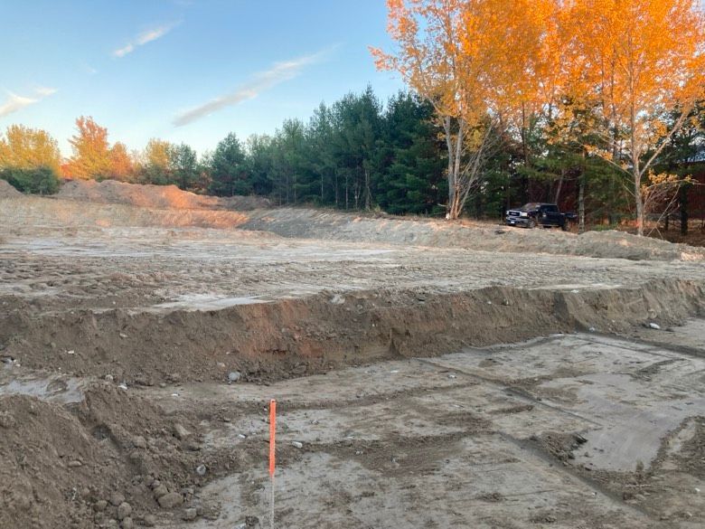 A dirt field with trees in the background and a red pole in the middle.