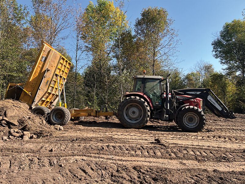 A tractor is loading a dump truck with dirt in a dirt field.