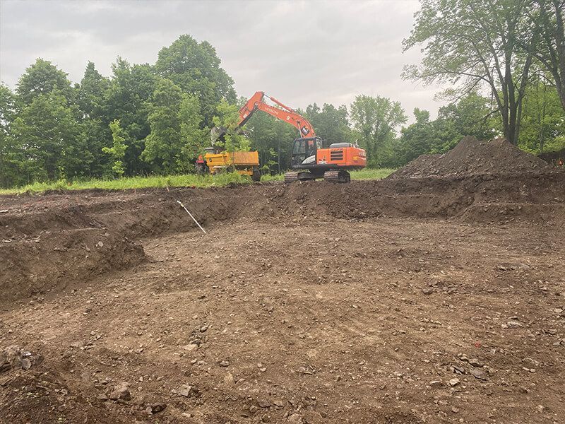 A large orange excavator is digging a hole in a dirt field.