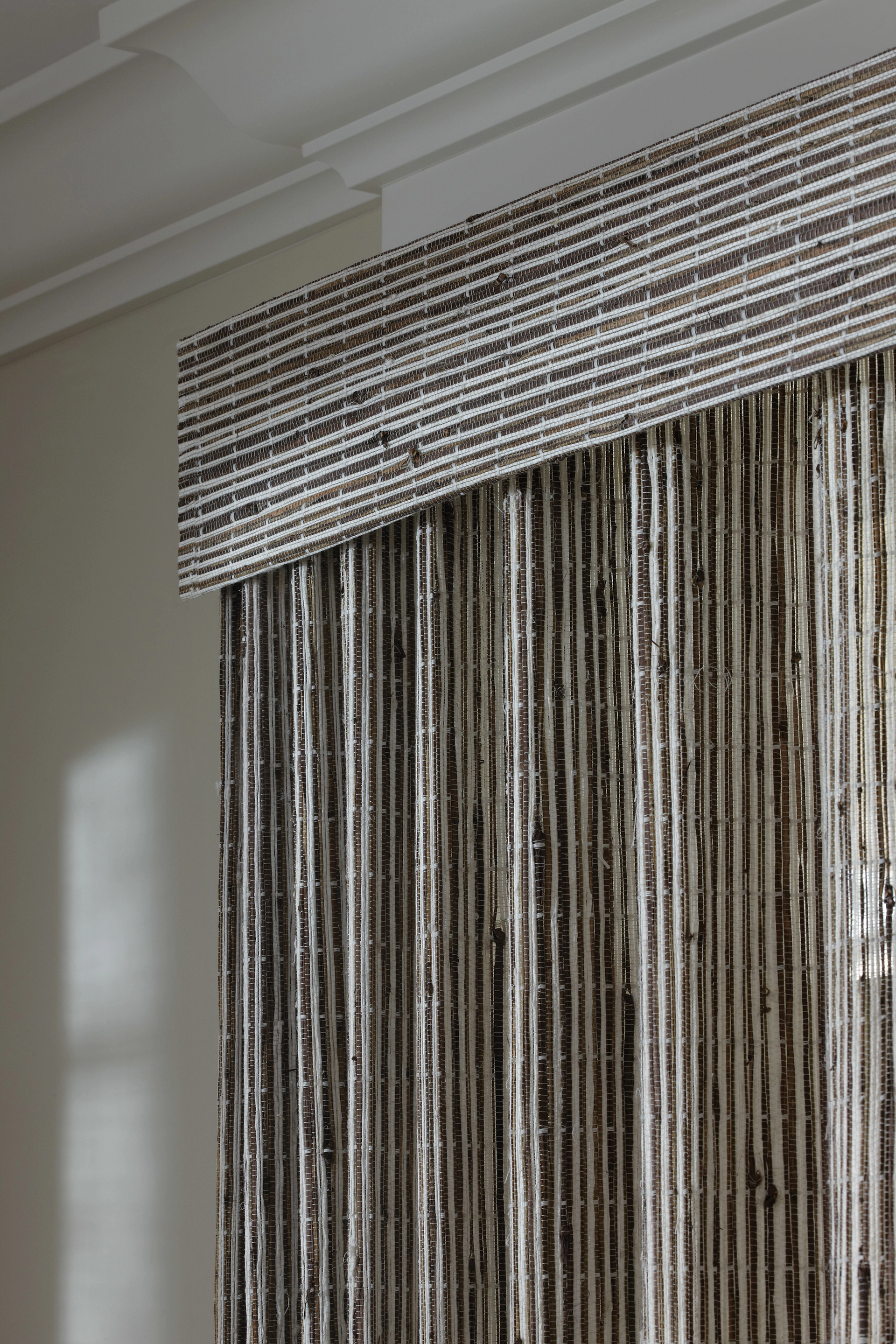 A close up of a window with a striped curtain and a cornice.