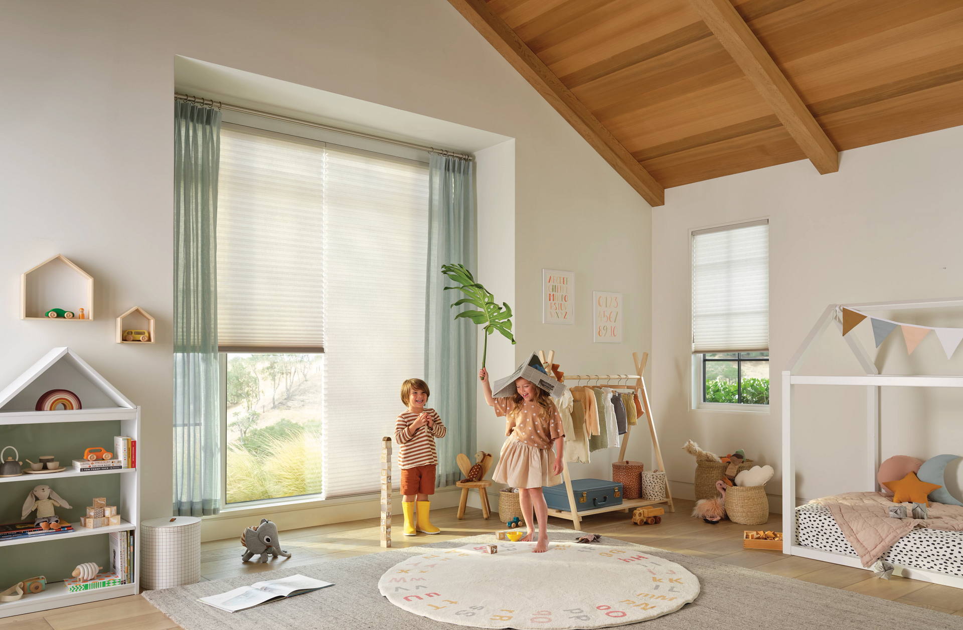 Two children are playing in a play room with a bed and a window.