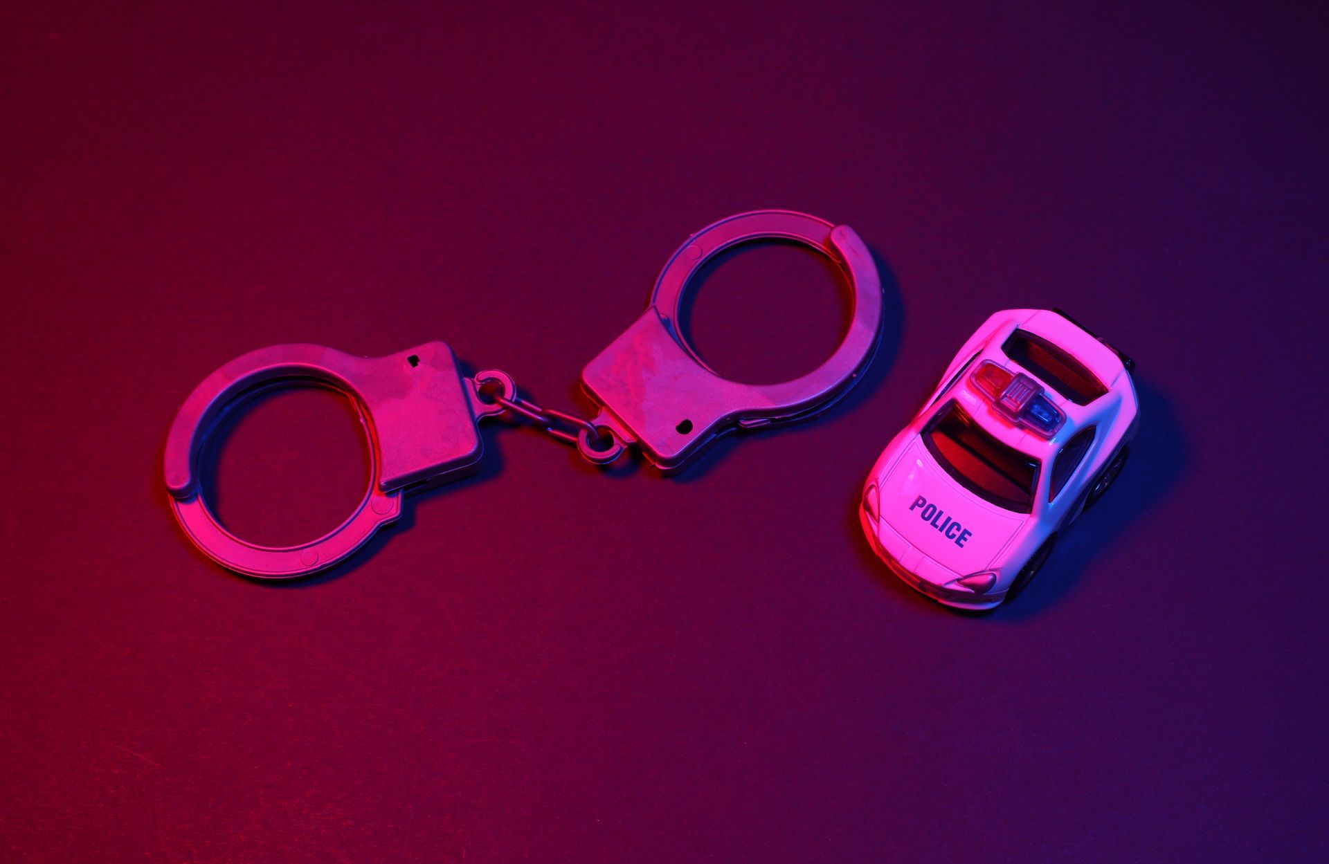 Pink handcuffs beside a pink toy police car on a dark background