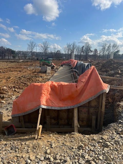 A man is pouring concrete on a sidewalk with a shovel.