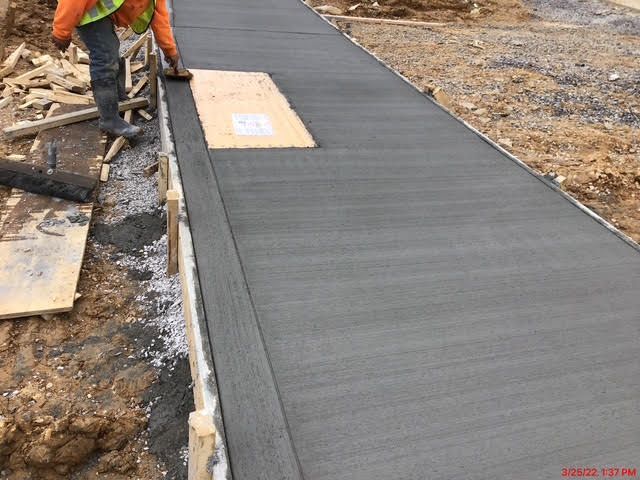 A construction worker is laying concrete on a sidewalk.