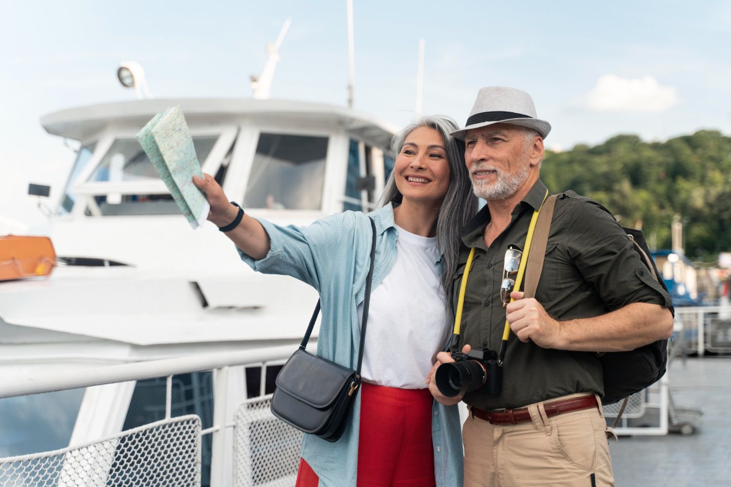 Two travelers point toward a map while standing on a boat deck, with a camera hanging around the man's neck.