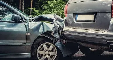 A dark grey car is shown with severe front-end damage after rear-ending another grey vehicle on a road.