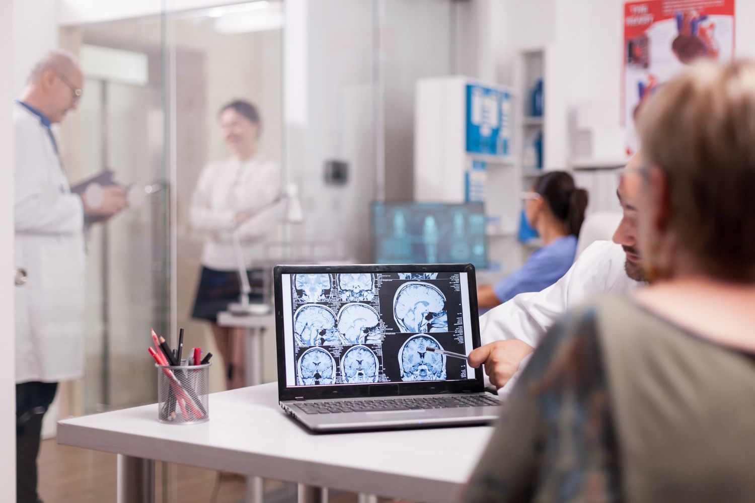 Medical professionals look at a brain scan on a laptop during a consultation in a brightly lit, modern office setting.