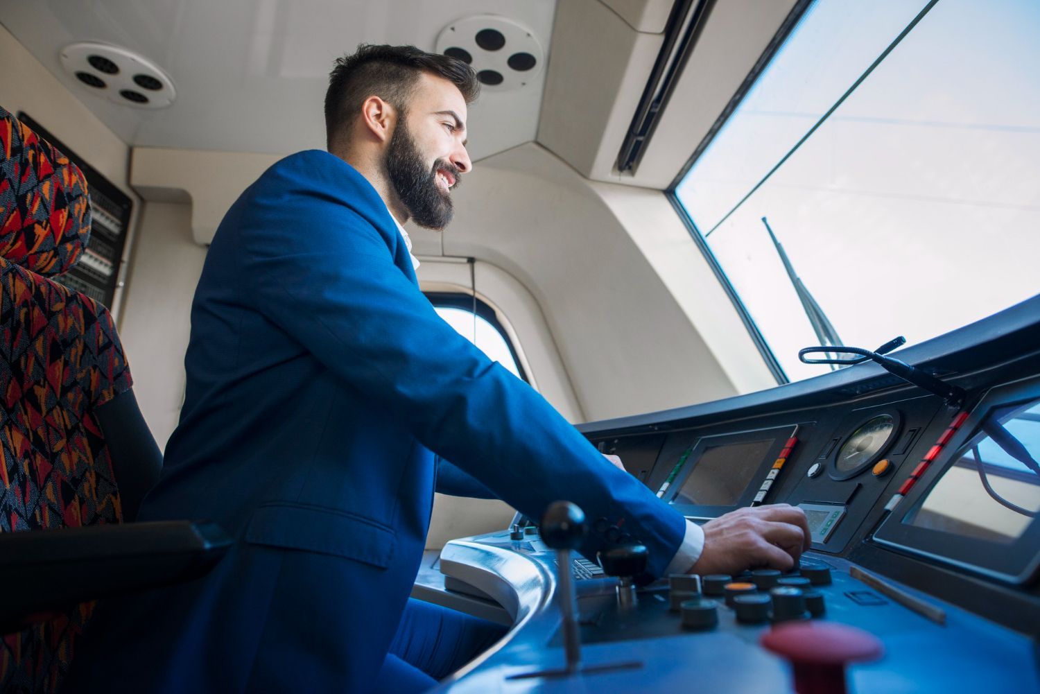 A person in a blue blazer operates a train control panel in the driver's cabin.