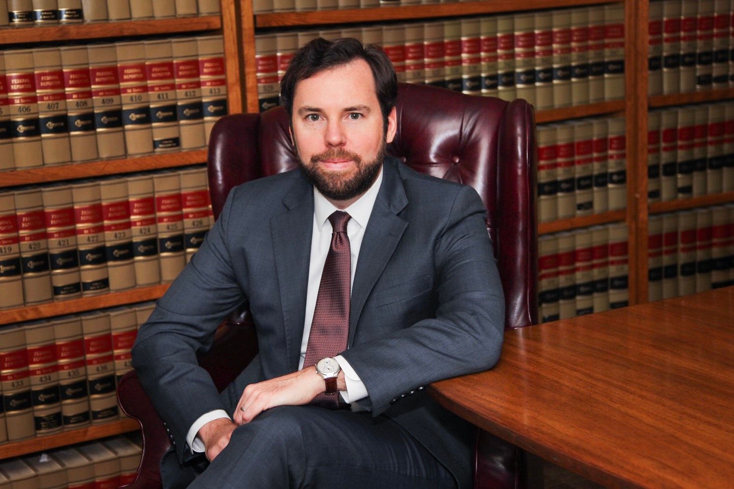 A professional seated in a leather chair in a law library with bookshelves in the background.