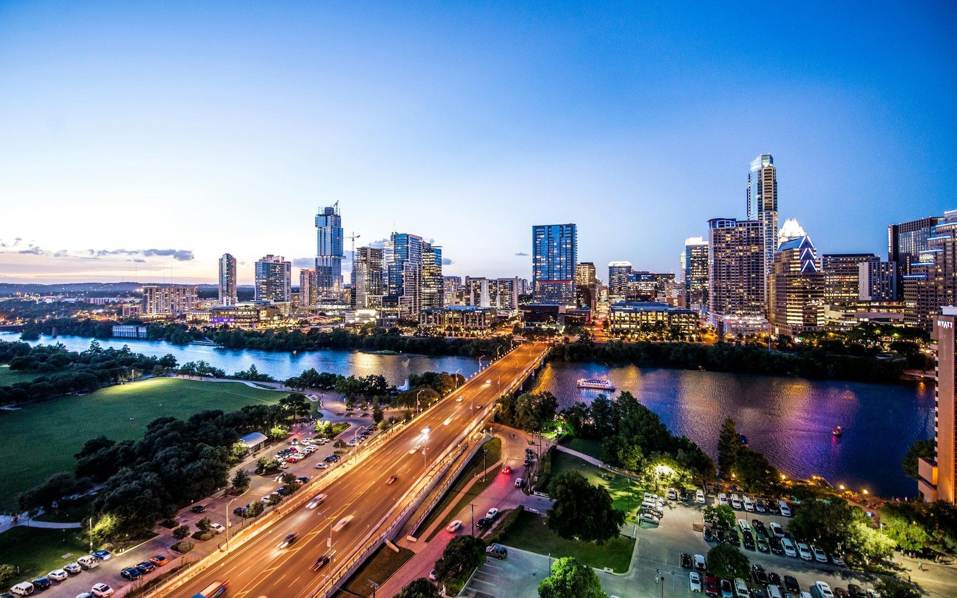 A twilight aerial view of the Austin, Texas skyline, featuring the Congress Avenue Bridge spanning Lady Bird Lake.