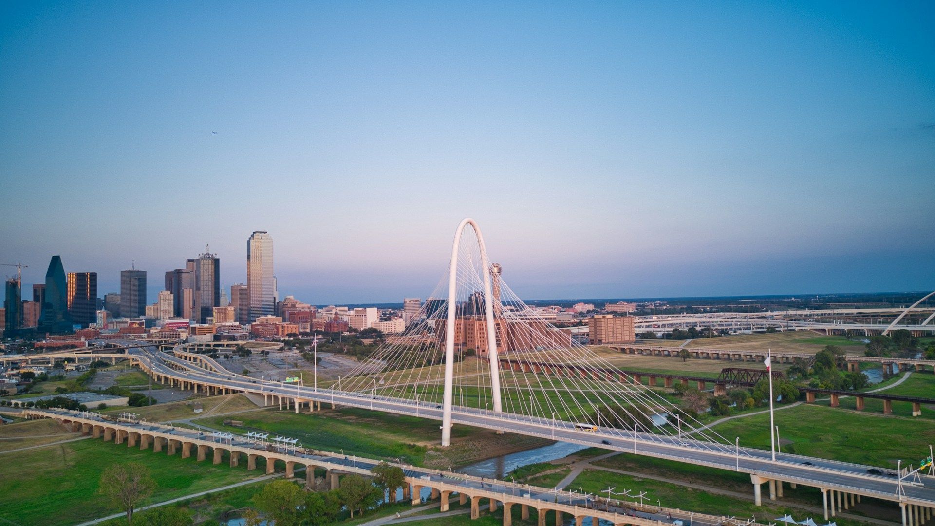A high-angle view of the Dallas skyline with the Margaret Hunt Hill Bridge spanning the Trinity River at dusk.