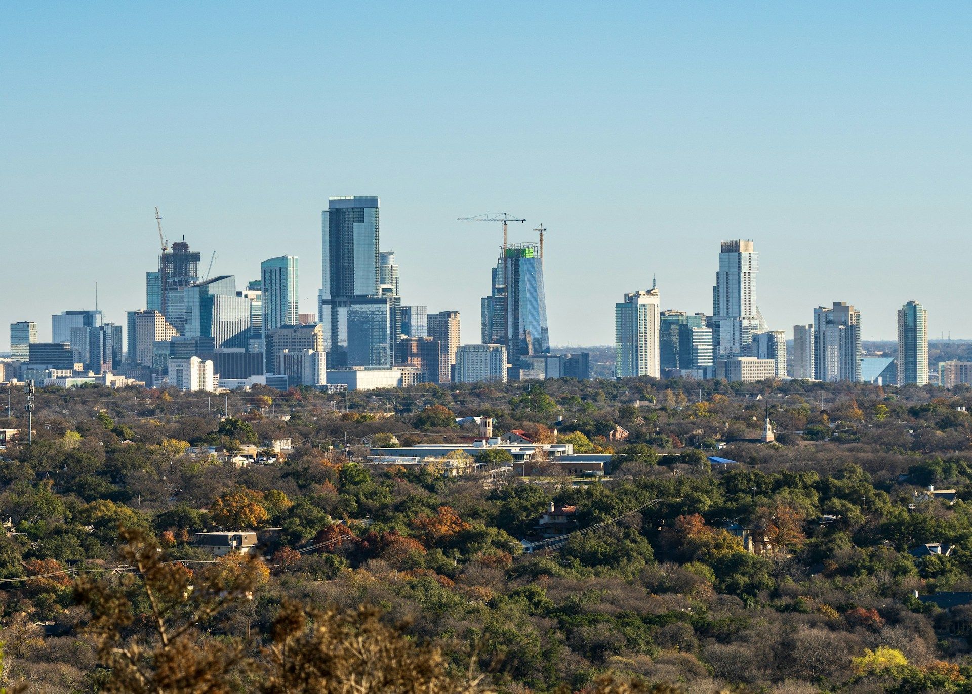 A distant view of the Johannesburg skyline rising above a dense, tree-covered landscape under a clear blue sky.