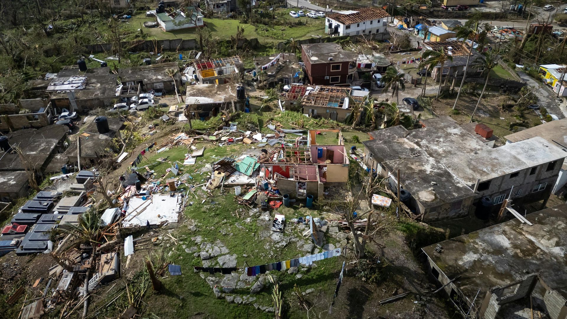 An aerial view of a residential area destroyed by a natural disaster, with damaged buildings and debris scattered about.
