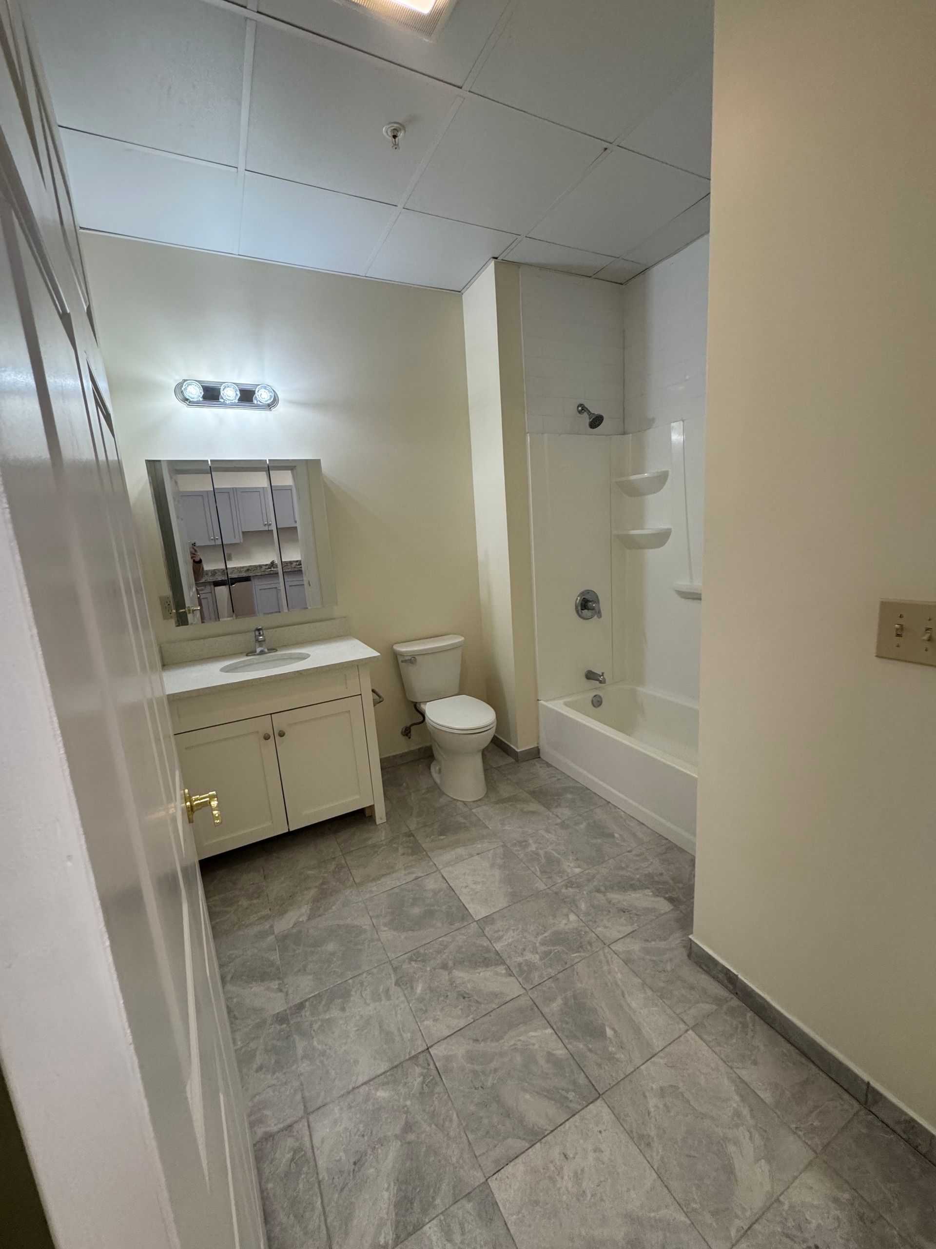 Bathroom with white vanity, toilet, bathtub, and gray tiled floor.