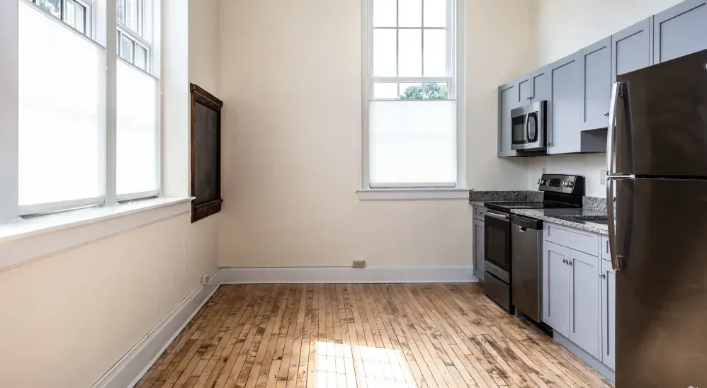 Kitchen with stainless steel appliances, grey cabinets, hardwood floors, and large windows.
