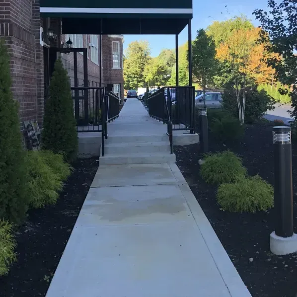 Sidewalk leading to a building entrance with awning, landscaping, and handrails.