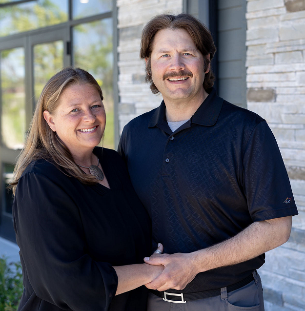 A smiling couple Courtney and Cory Wiest standing in front of a building — St Michael, MN — EMEX Benefits Systems