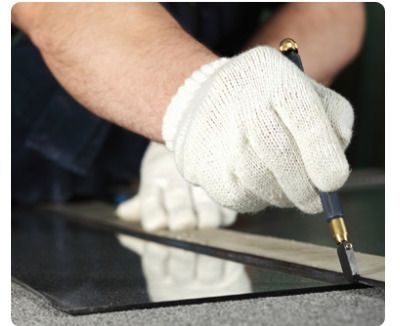 Persona che indossa guanti bianchi mentre incide il vetro con un tagliavetro.