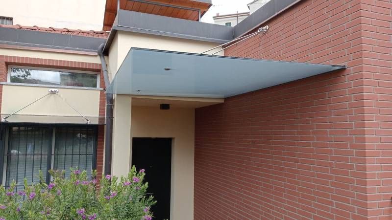 Ingresso di un edificio moderno con una pensilina rettangolare minimalista sopra la porta. Mattoni rossi e parete beige.