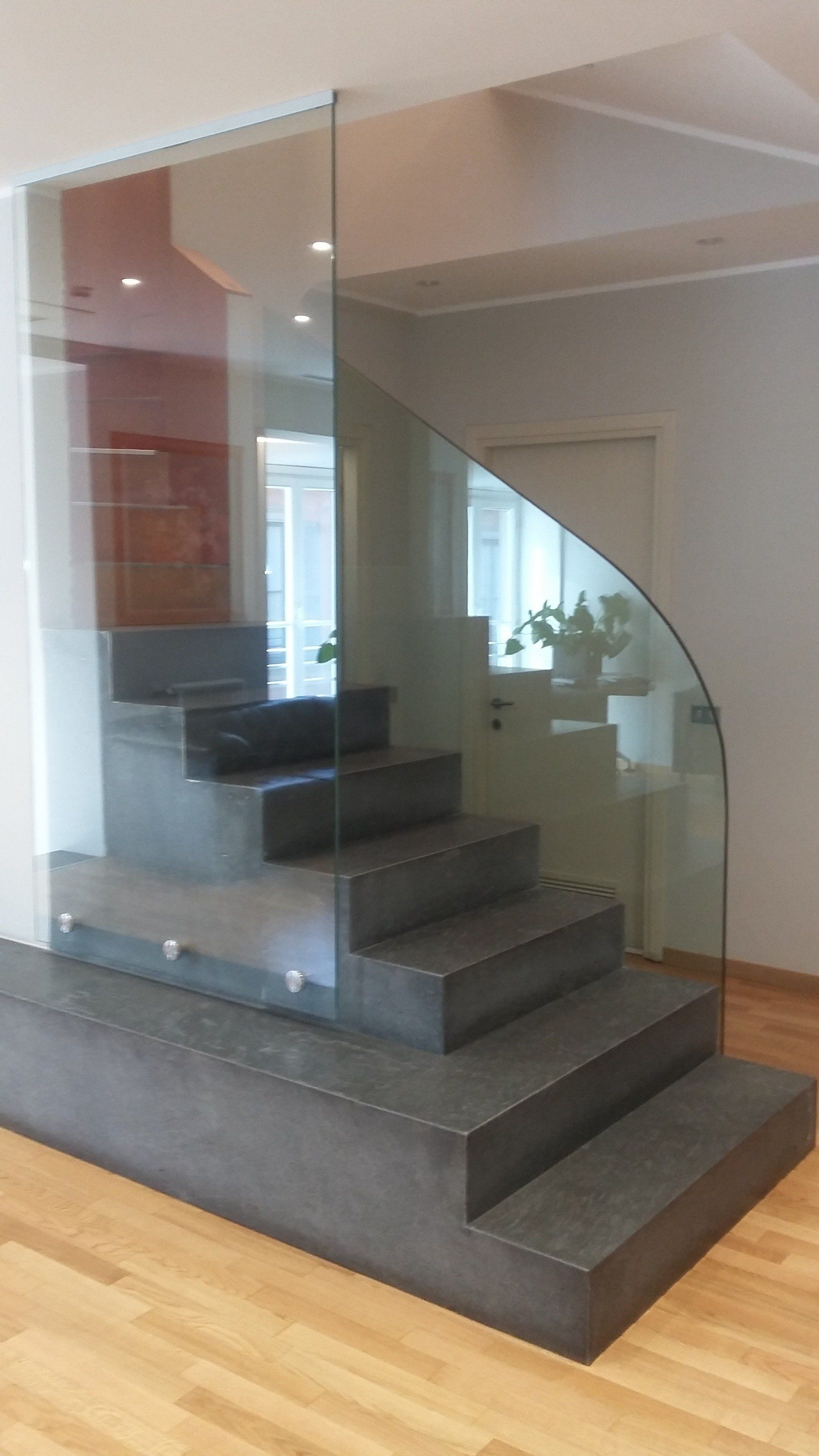 Scale in pietra grigia con ringhiera in vetro curvo in una casa moderna.