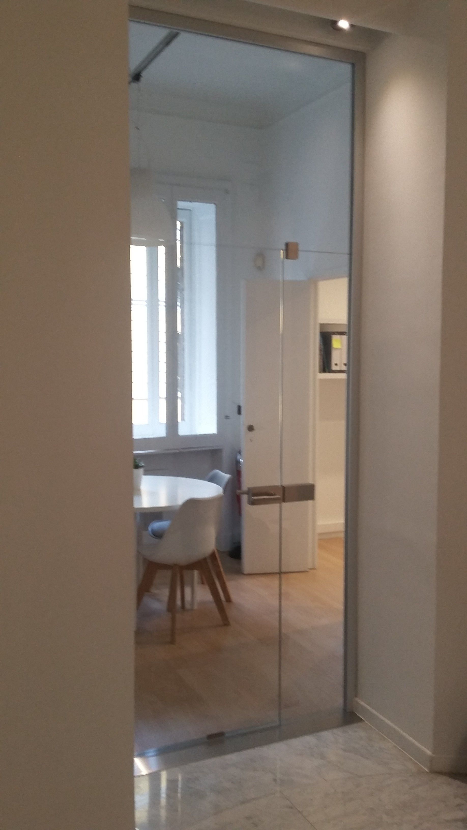 Porta a vetri su un ingresso, che riflette una stanza con un tavolo, delle sedie e una finestra.