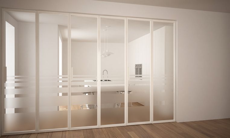 Due stanze bianche sono separate da porte scorrevoli in vetro, con strisce orizzontali satinate.