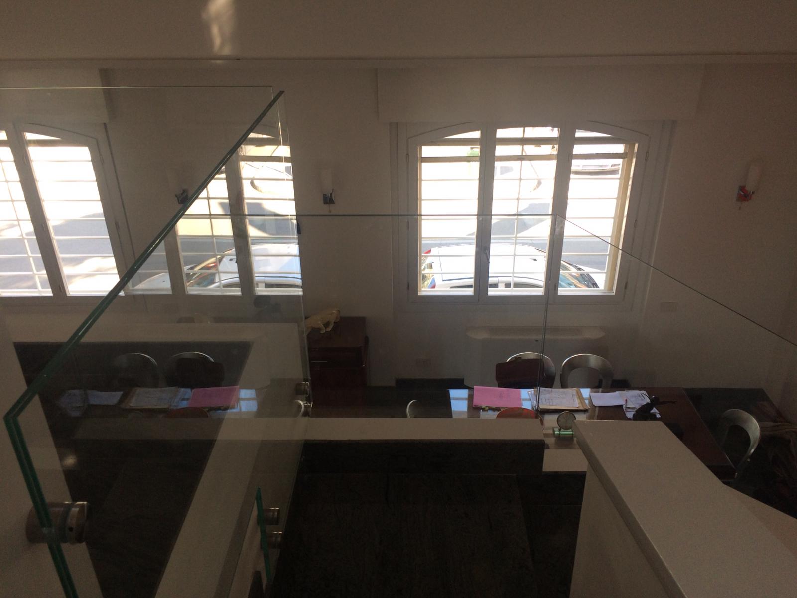 Vista dall'alto di uno spazio ufficio ben illuminato, con finestre, scrivanie e sedie.