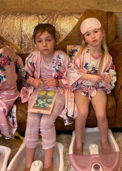 Two little girls are sitting on a couch with their feet in a foot spa.