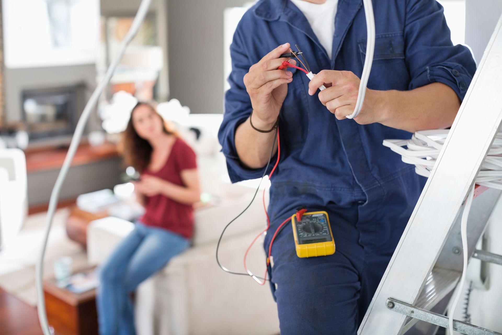 An electrician, in a blue uniform, performing residential electrical services in the living room.