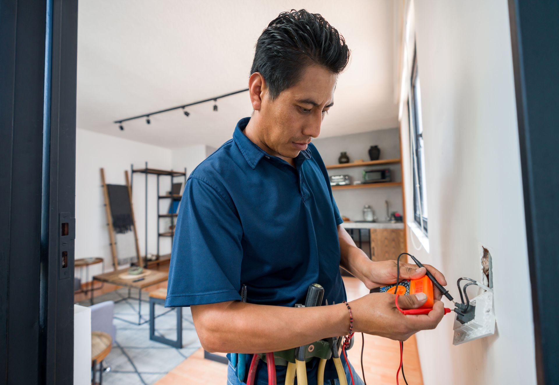 Technician testing electrical outlet with multimeter inside a modern home interior room setting area.