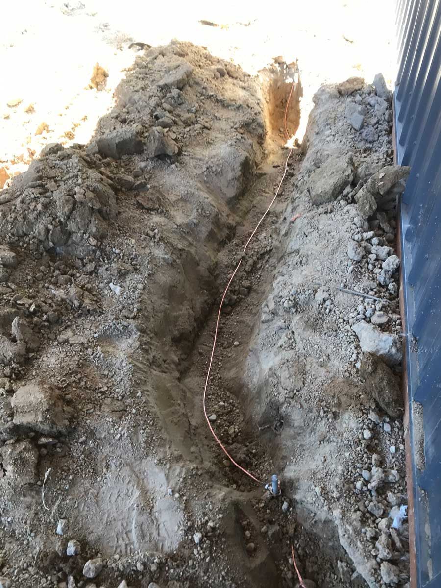 A copper wire is laying in the dirt next to a wall.
