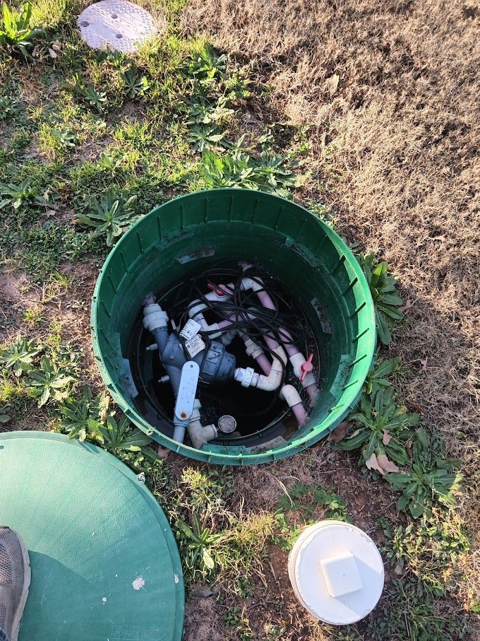 A green bucket filled with water and pipes is sitting in the grass.