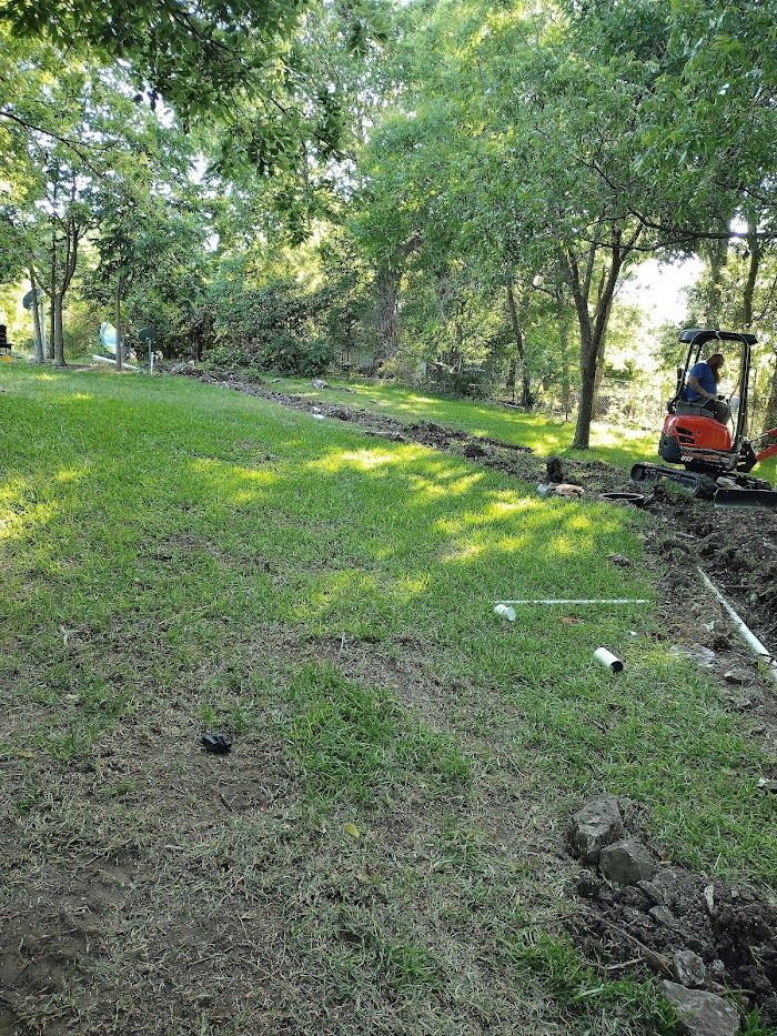 A red excavator is digging a hole in the grass in a park.