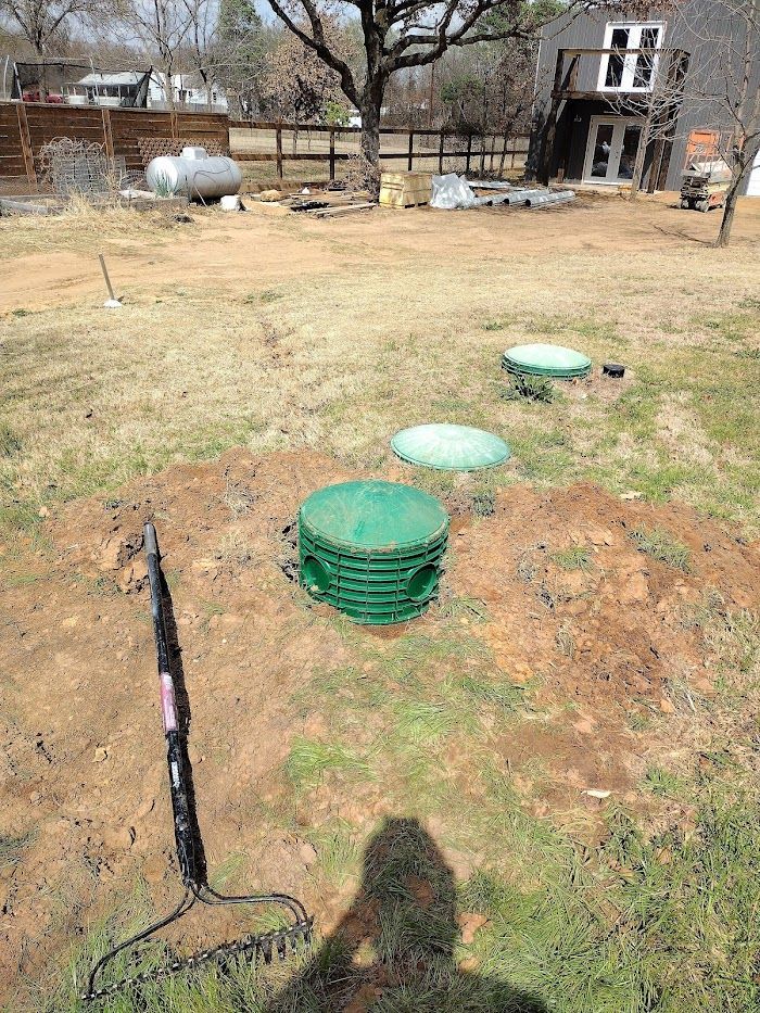 A rake is sitting in the middle of a field next to a septic tank.