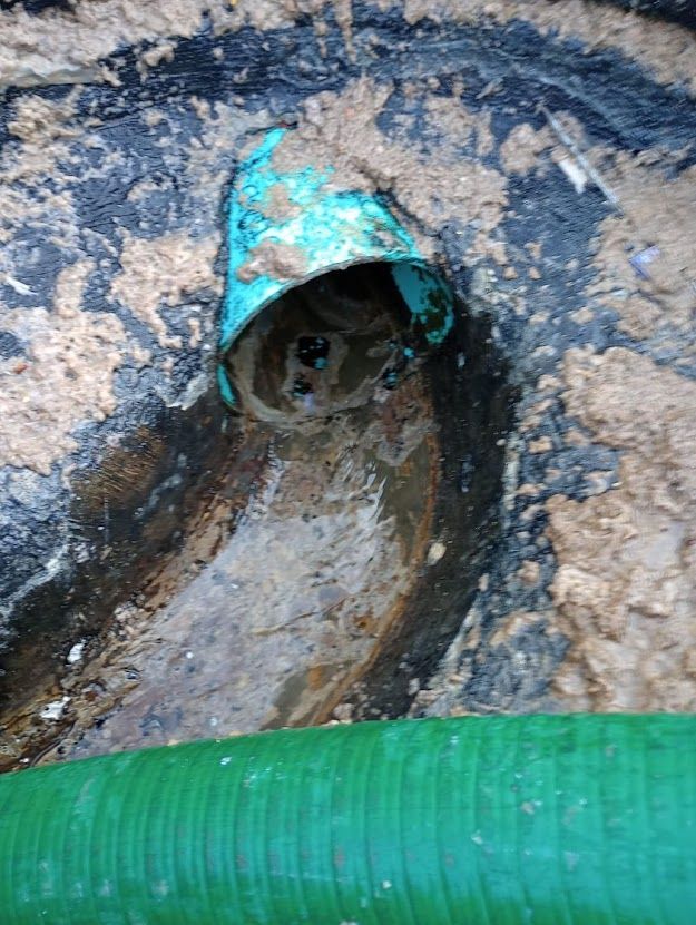 A green pipe is sticking out of a hole in the ground.