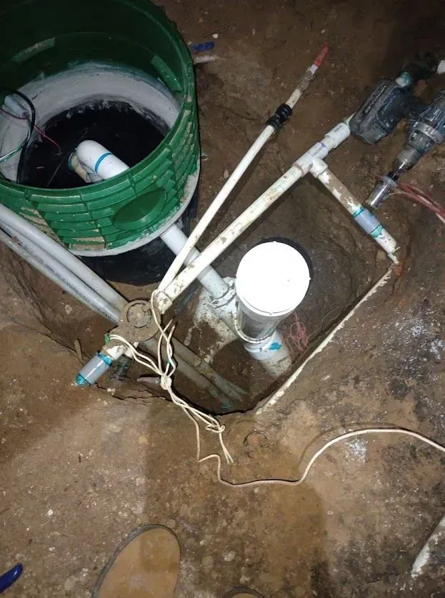 A green bucket is sitting in the dirt next to a white pipe.