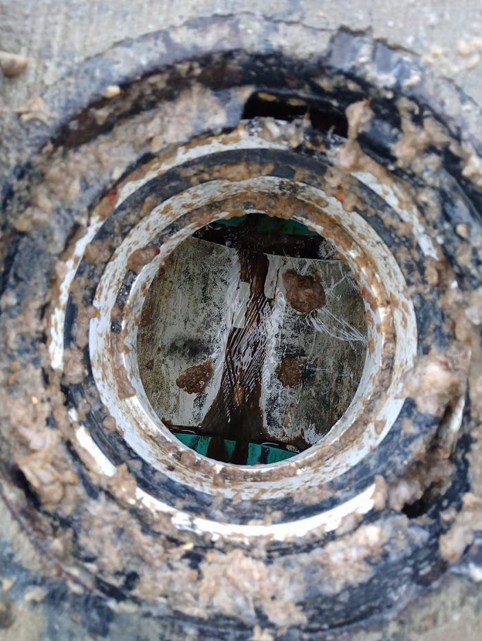 A close up of a dirty manhole cover with a hole in it.