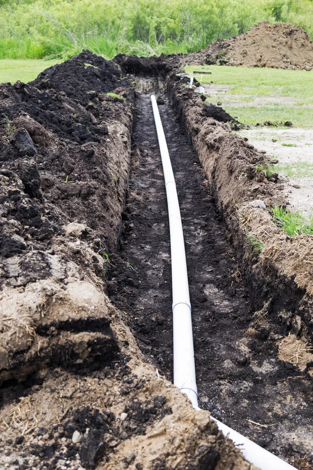 A white pipe is being installed in a trench in the dirt.