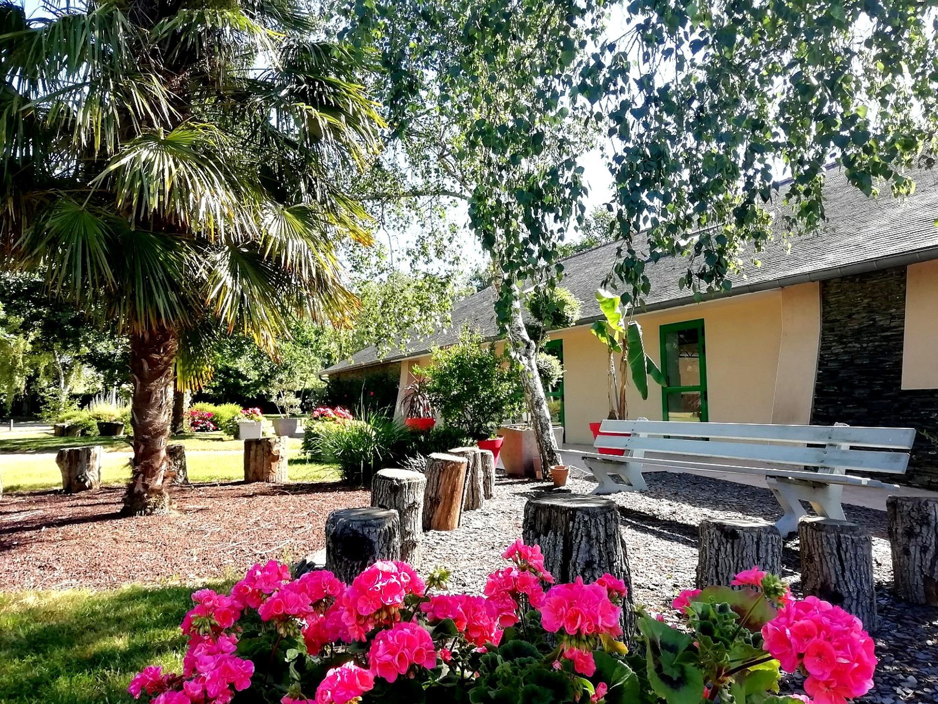 Une maison avec un banc blanc et des fleurs roses devant.