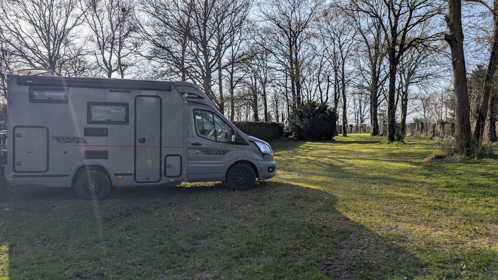 Un camping-car est garé dans un champ herbeux entouré d'arbres.