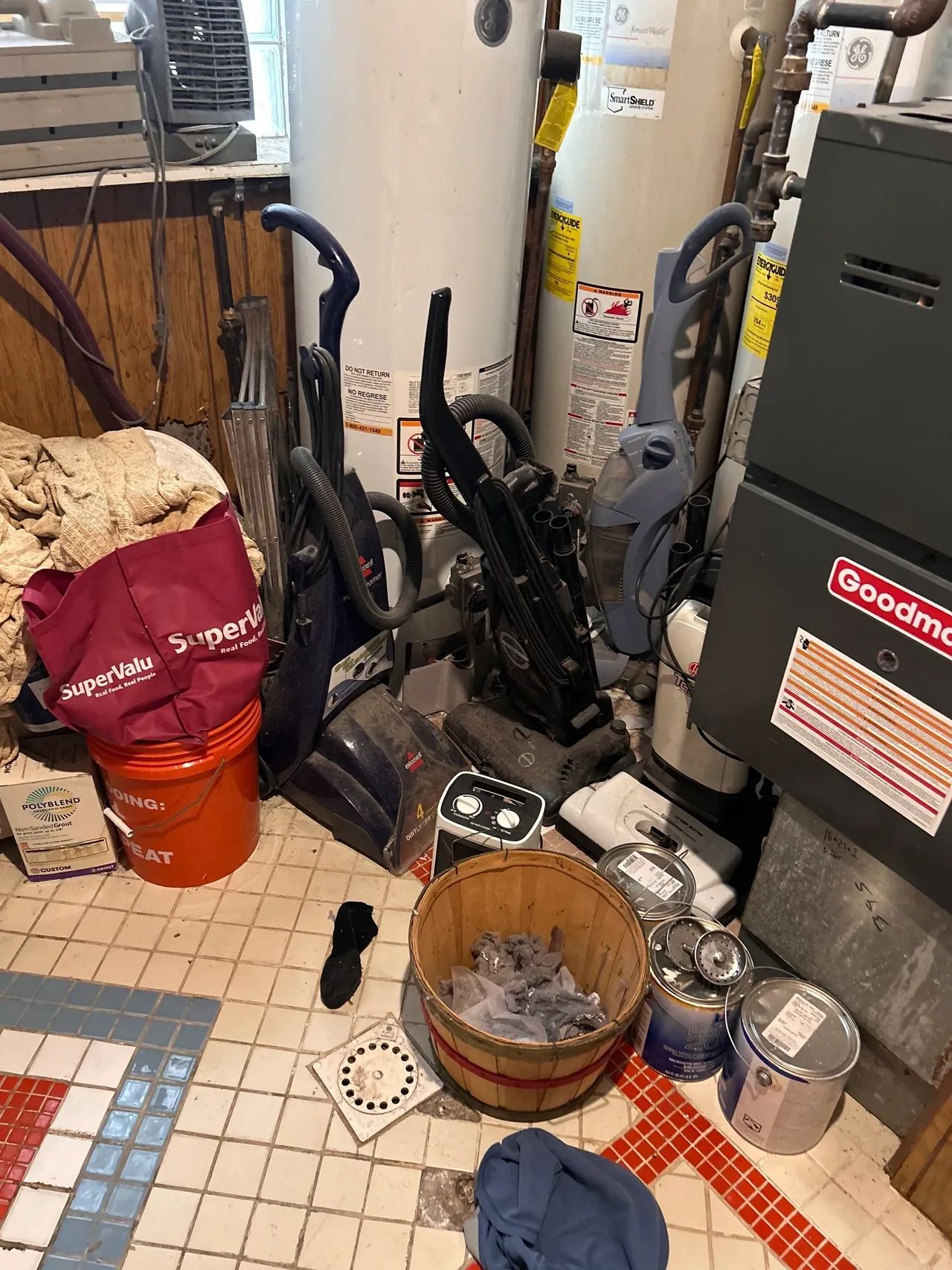 A vacuum cleaner is sitting on a tiled floor next to a water heater.