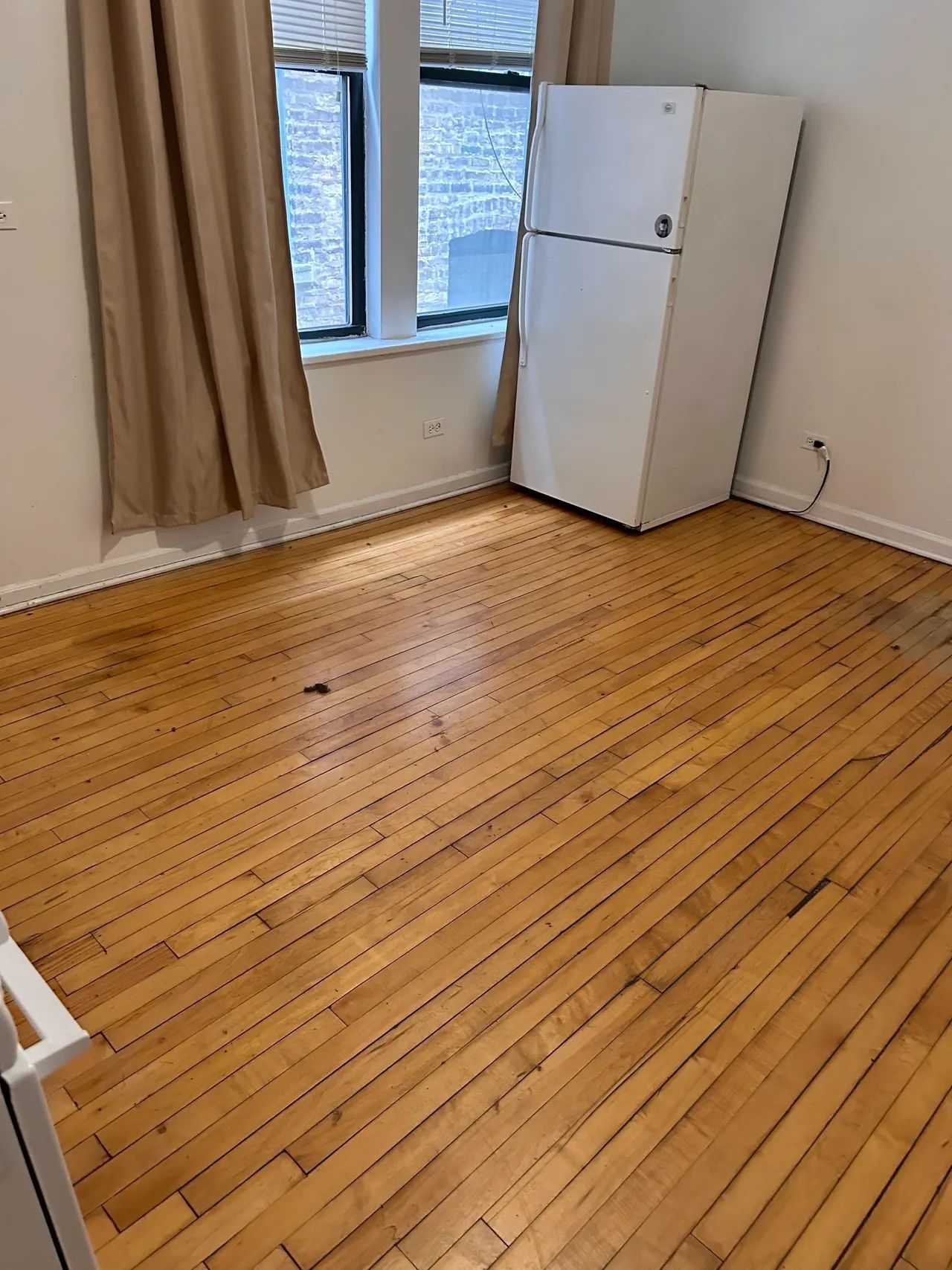 A room with a wooden floor and a white refrigerator.