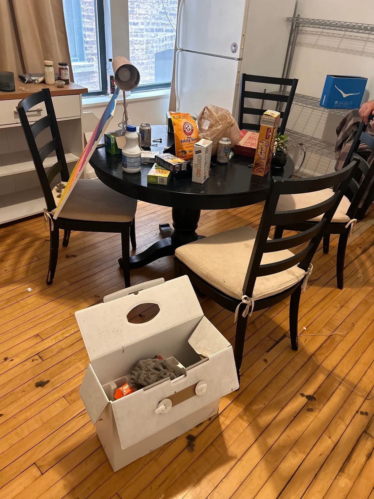 A messy dining room with a table and chairs and a box on the floor.