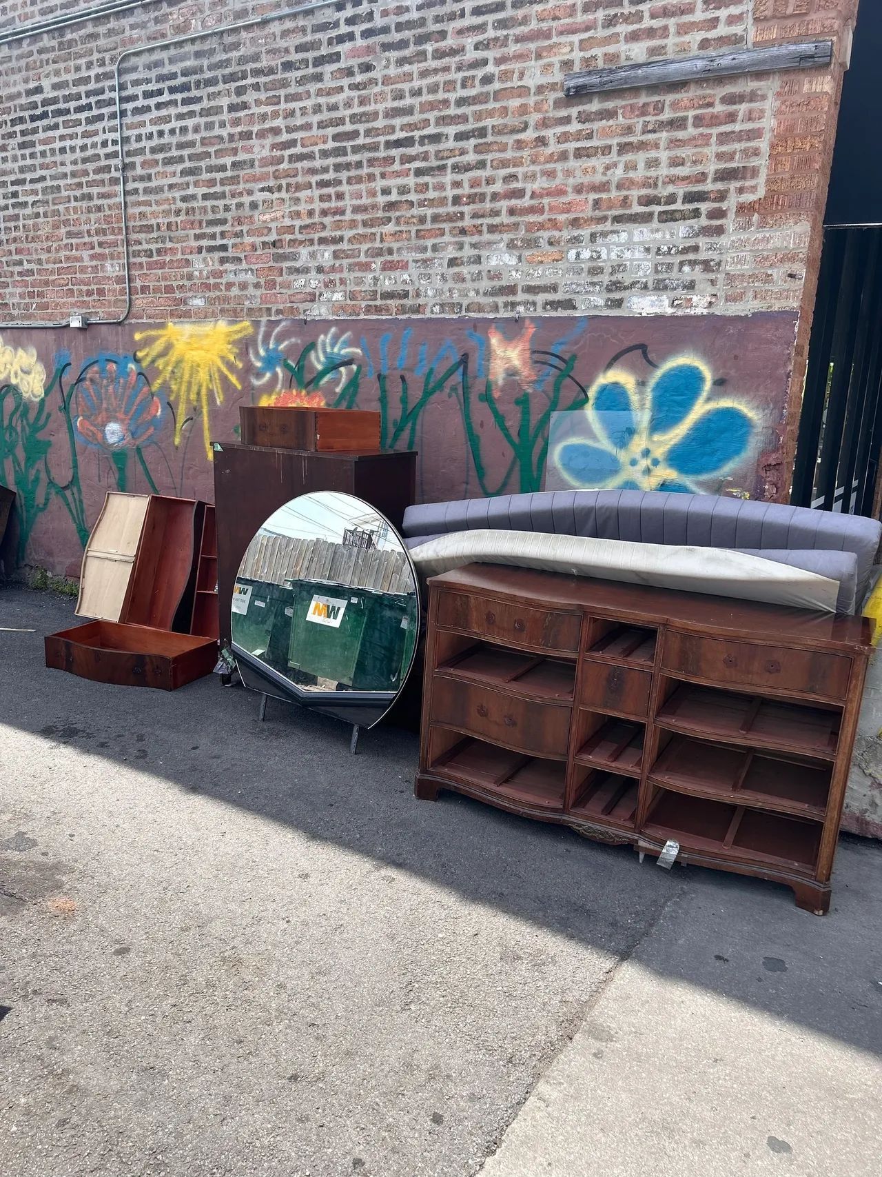 A bunch of furniture is sitting on the side of the road in front of a brick wall.