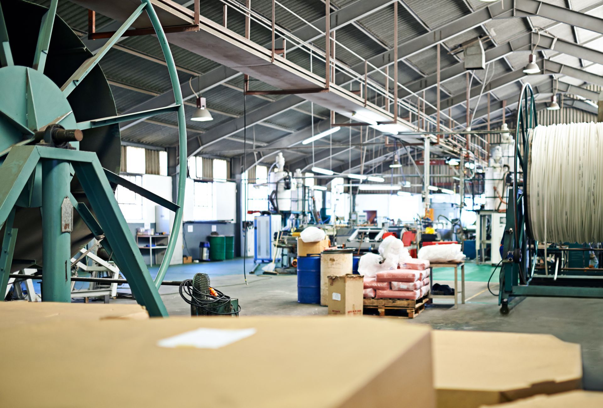 Industrial factory interior with large spools of material, boxes, and machinery.