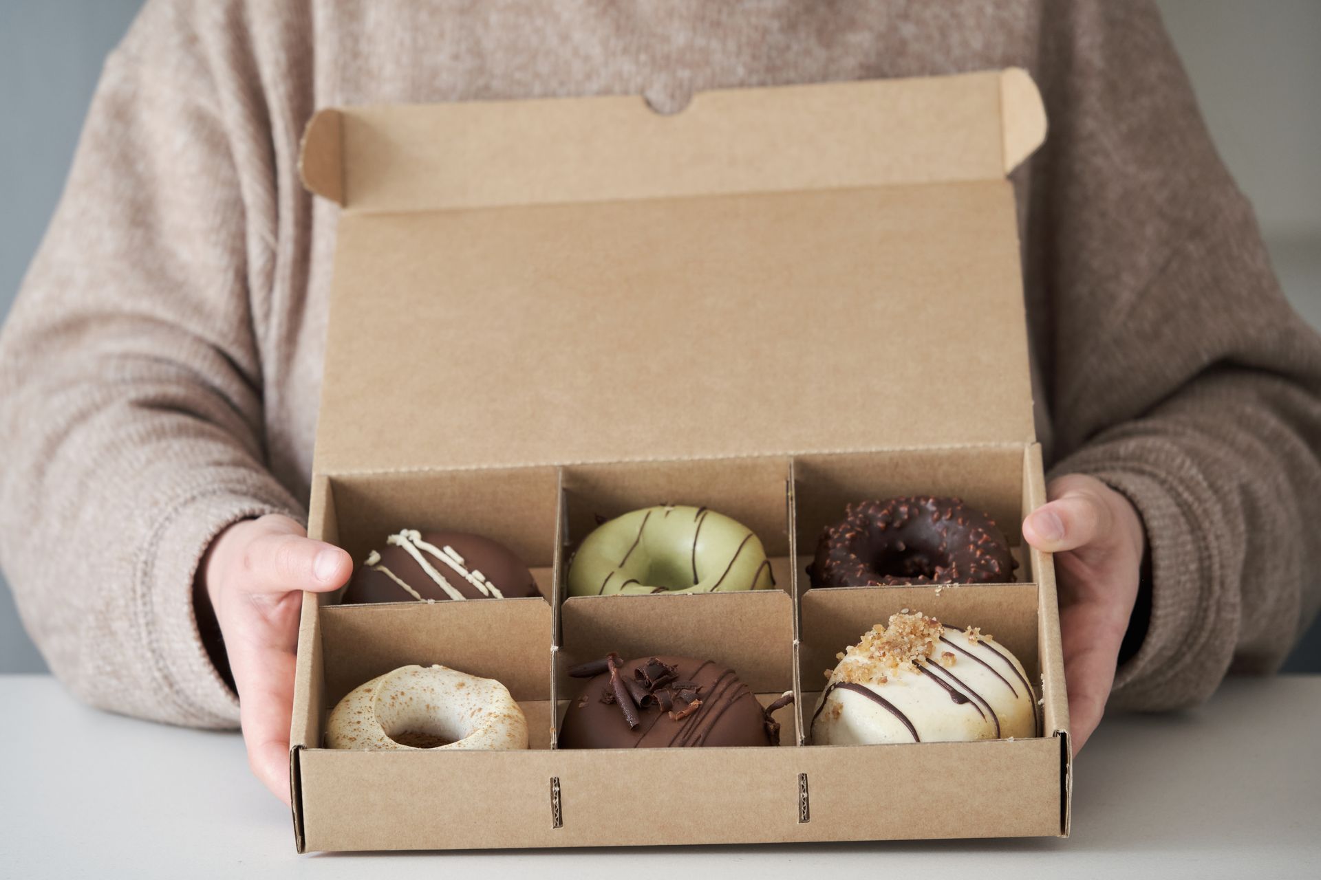 Person holding a cardboard box of six assorted donuts.
