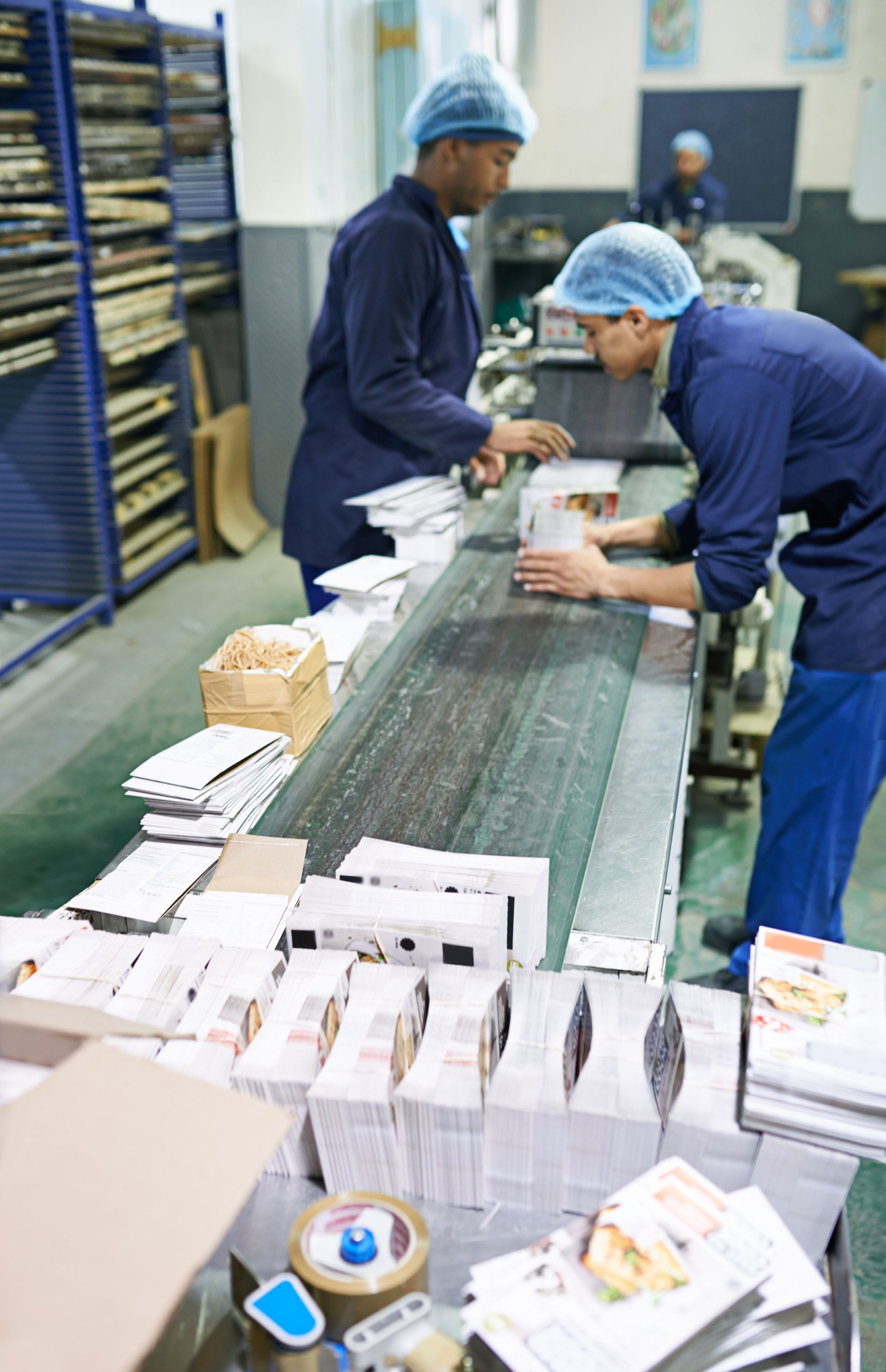 Workers in blue uniforms sort mail on a conveyor belt in a processing facility.
