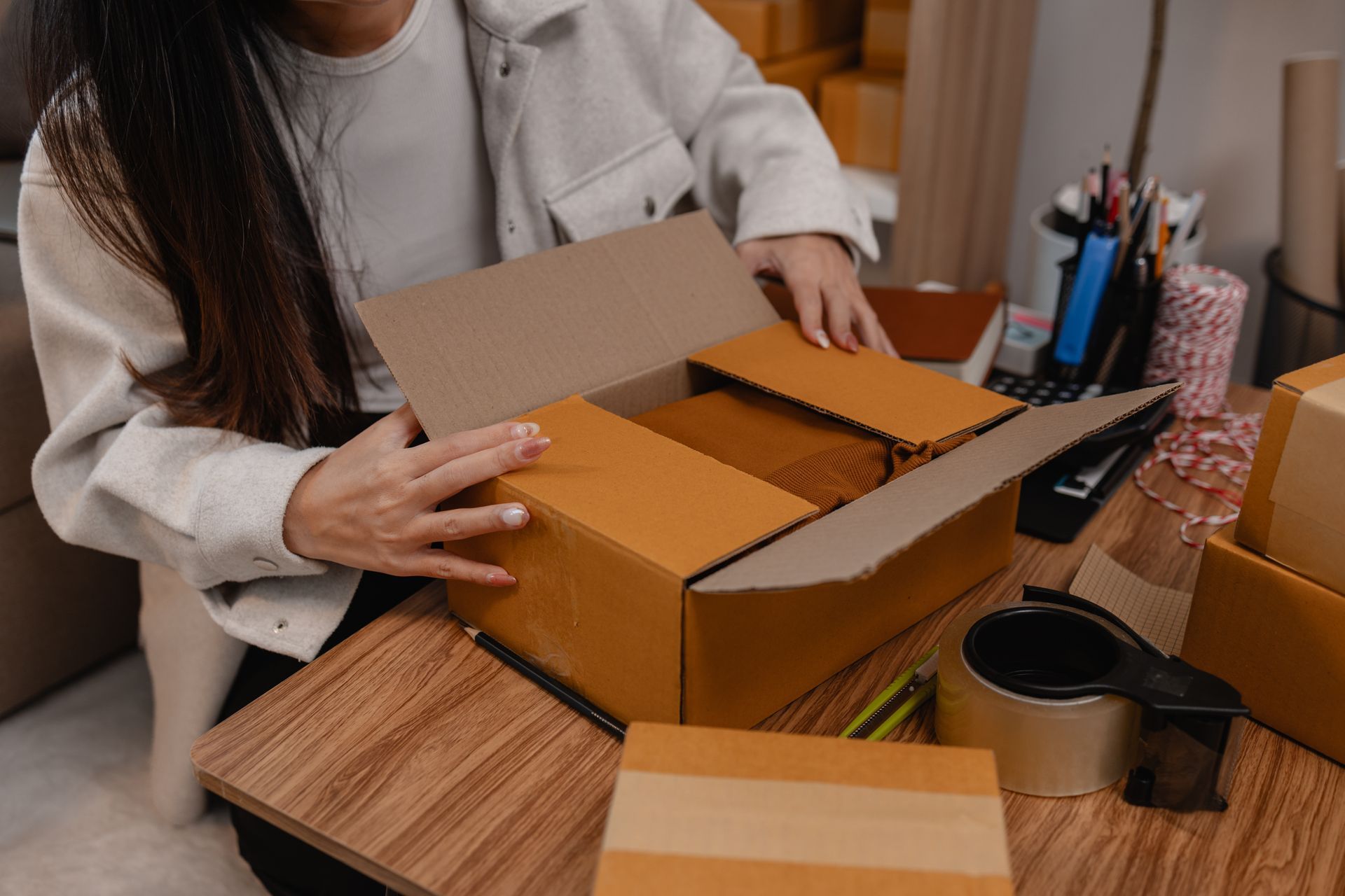 Person packing items into a cardboard box on a wooden desk.